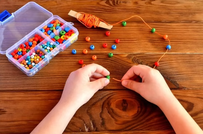Close-up of child hands practicing fine motor skills with beads and crafts at home